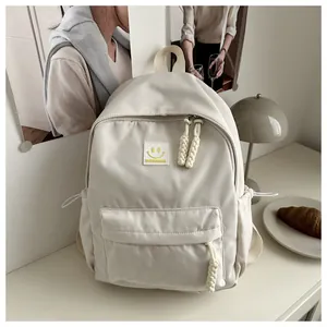 Detalle de una mochila crema minimalista con parche de cara sonriente y bolsillo con cordón
