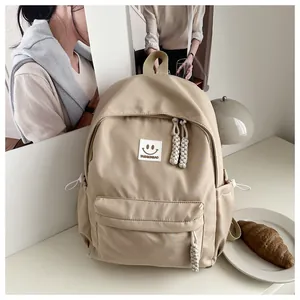 Detalle de mochila de nylon beige con parche de cara sonriente y tiradores de cuerda