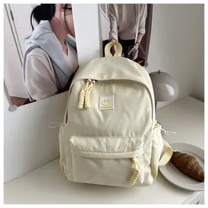 Detalle de mochila de nailon crema con tiradores trenzados y parche de sonrisa