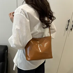 Brown glossy shoulder bag with silver bow detail worn by a model in casual setting