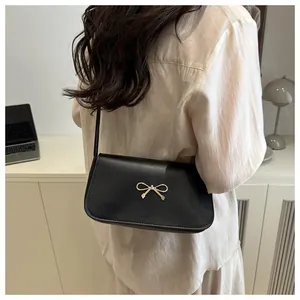 Detail of a black leather underarm bag featuring a delicate golden bow clasp decoration