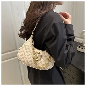 Detail van crème schoudertas met bruine M-patronen en gouden ketting op een model
