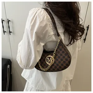 Detail of dark brown underarm bag with M-pattern print and gold chain strap