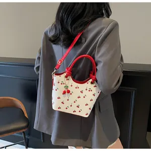 Detail of white bucket bag with red cherry prints and red knotted handles on model
