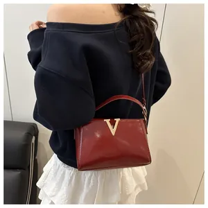Dettaglio della borsa a tracolla in vernice rossa con hardware a V dorato su modella