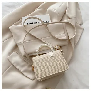 Detail van beige gevlochten tas met parelhandvat op blazer, fijne textuur en gouden haken