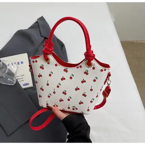 Detail of white bucket bag featuring red cherry prints and contrast red handles on a bed