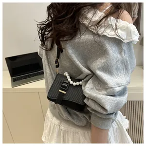 Detail van zwarte crossbodytas met geweven textuur, gesp en parelmoer handvat