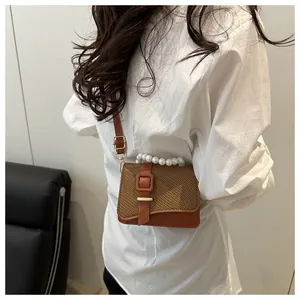 Detail van bruine geweven crossbodytas met parelhandvat en goudkleurige gespsluiting