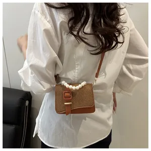 Detail van een bruine geweven crossbodytas met parelhandvat en leer op een model