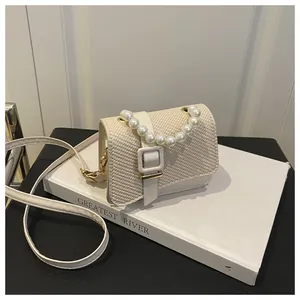Detail van crème geweven mini-tas met parelketting en lederen schouderriem