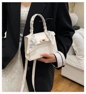 Detailed shot of white faux crocodile leather handbag with elegant silk scarf wrap on handle