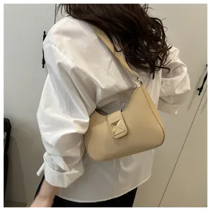 Detailed view of cream leather shoulder bag with gold pyramid buckle worn by a model