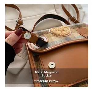 Detail showing the magnetic snap closure on the brown plaid backpack with a teddy bear