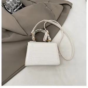 Close-up of white crocodile pattern crossbody bag with decorative silk scarf and strap