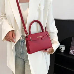 Deep red trapezoid handbag with dual handles and gold accents in a stylish crossbody design