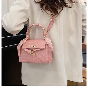 Pink croc-embossed square handbag featuring a metal turn-lock and scarf-wrapped handle