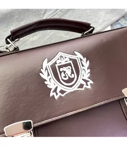 Close-up of dark brown leather bag with white embroidered school badge and silver buckle