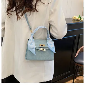 Detail of light blue crocodile-embossed handbag with silk scarf handle and gold hardware