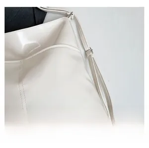Detailed macro view of cream patent leather texture and fine stitching on a tote bag
