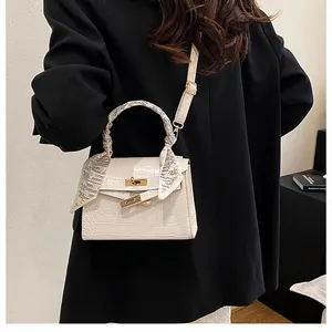 Detailed view of white crocodile pattern bag with golden lock and silk scarf handle decor