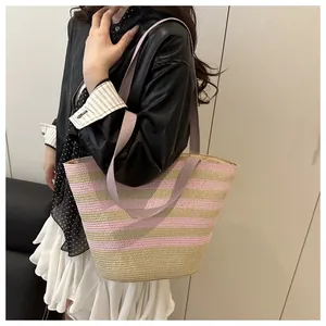Close-up of woven straw tote bag featuring pink and beige stripes and purple straps