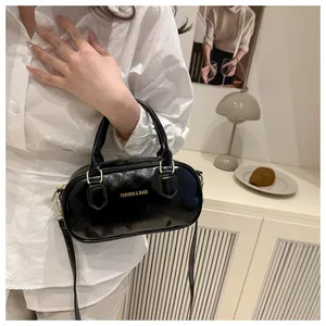 Detail of a black patent leather mini Boston bag with gold hardware and shoulder strap