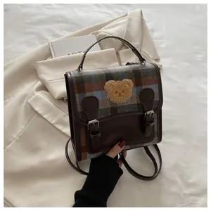 Detailed shot of plaid tweed handbag with plush bear patch and leather buckle accents