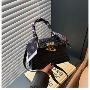 Close-up of black crocodile pattern handbag with gold twist lock and heart print scarf handle