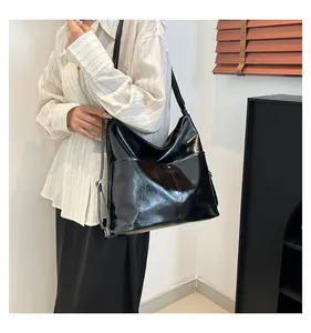Detail of a black patent leather tote bag with large front pockets and glossy finish