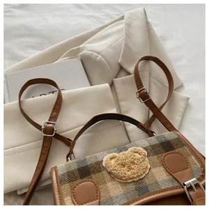 Close-up of a checkered fabric bag with a plush teddy bear patch and brown leather straps