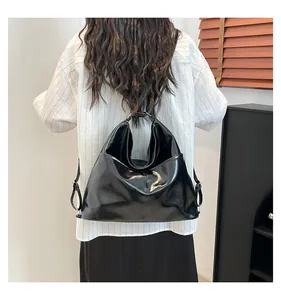 Detail of glossy black tote bag with slender adjustable strap worn by a model