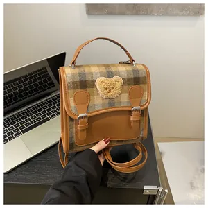 Close-up of vintage brown plaid backpack with a teddy bear patch and metal buckles