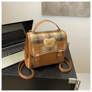 Detail of British style plaid handbag with a 3D plush bear on textured desk