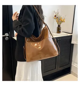Brown glossy patent leather tote bag shown on shoulder to display its large capacity