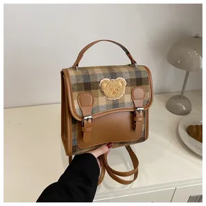 Close-up of vintage brown plaid backpack with cute teddy bear patch and metal buckle
