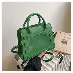 Dettaglio della borsa a mano verde in PVC e pelle posta su una valigia bianca