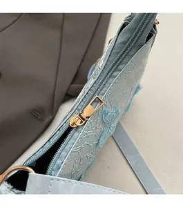 Detailed close-up of smooth metal zipper and floral lace embroidery on light blue bag