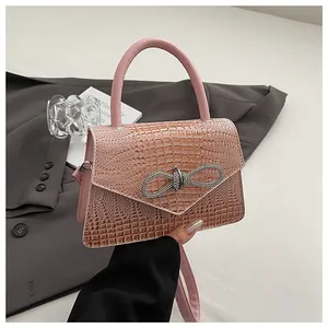 Detail of pink crocodile texture handbag with sparkling bow buckle and leather handle
