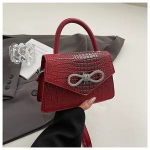 Detail of red crocodile textured mini bag with silver rhinestone bow and envelope flap