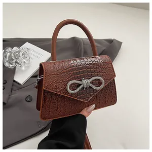 Detail of dark brown crocodile texture handbag with sparkling rhinestone bow buckle