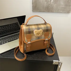 Brown leather plaid backpack with a teddy bear patch on a modern office desk