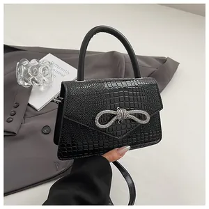 Detail view of black crocodile pattern leather bag with a crystal bow buckle on a suit