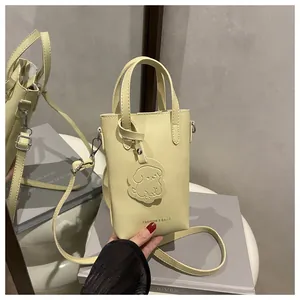 Detailed macro view of a light yellow leather crossbody bag with cute dog charm