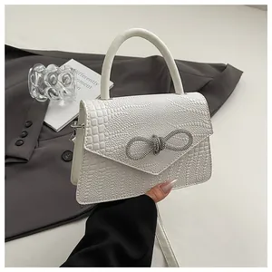 Detail of white crocodile embossed leather bag with rhinestone bow buckle and top handle