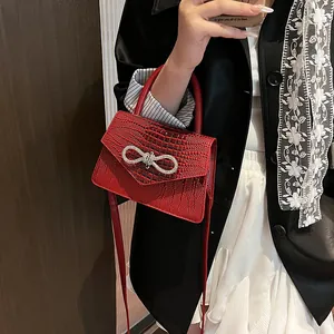 Red crocodile embossed mini bag with sparkling bow buckle and top handle held by model