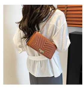 Sac bandoulière marron matelassé avec chaîne dorée porté par un mannequin en studio