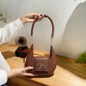 Dettaglio della borsa a mezza luna marrone con fiocco dorato e tracolla lunga