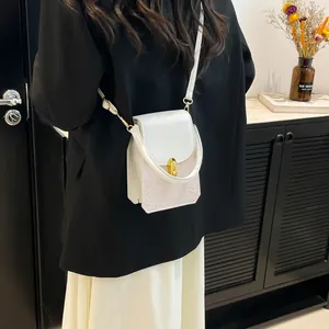 Mini white leather crossbody bag with gold lock and textured finish worn by a model