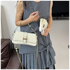 Détail du sac baguette crème avec texture en cuir plissé et bandoulière chaîne dorée